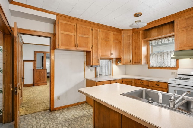 kitchen featuring white gas stove, under cabinet range hood, a sink, light countertops, and brown cabinets