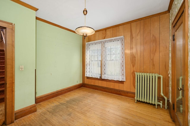 unfurnished room featuring radiator, ornamental molding, baseboards, wood-type flooring, and stairway
