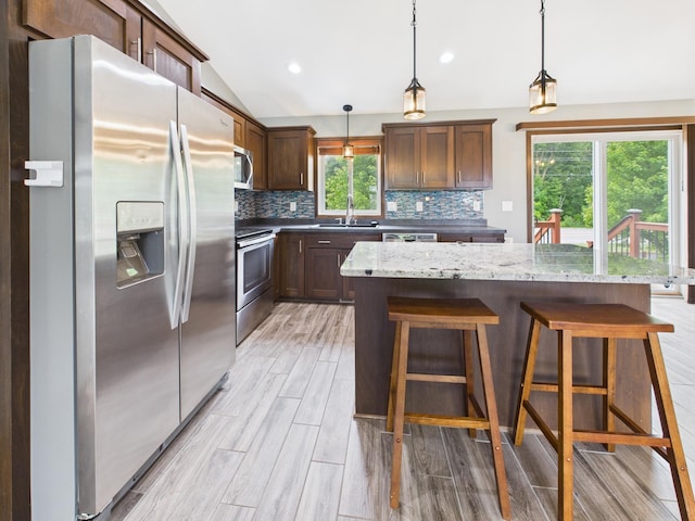 1214 Olivia St SE, New Prague, MN 56071 - kitchen featuring appliances with stainless steel finishes, backsplash, a center island, light wood-type flooring, and a breakfast bar area