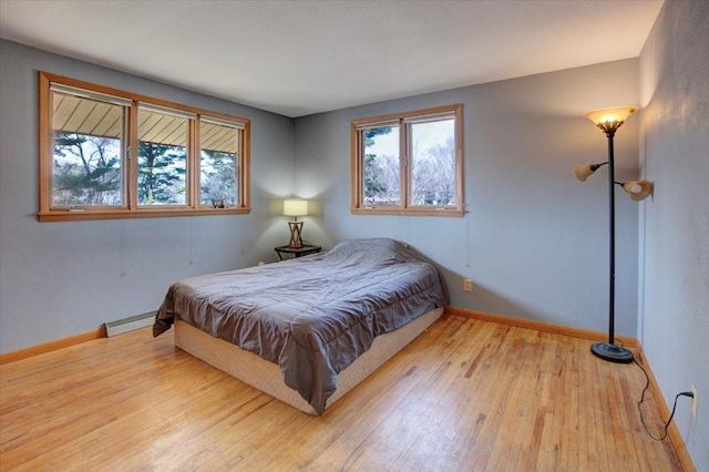 607 Cross Ave S, Amery, WI 54001 - bedroom featuring a baseboard radiator, multiple windows, baseboards, and wood finished floors