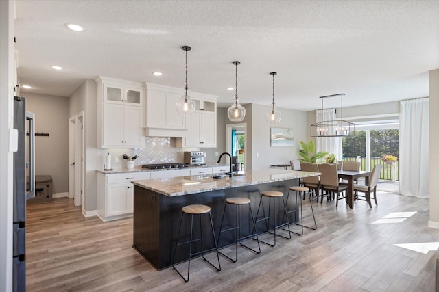 5360 Pine Island Rd, Woodbury, MN 55129 - kitchen featuring a sink, stainless steel gas cooktop, light wood finished floors, tasteful backsplash, and a kitchen breakfast bar