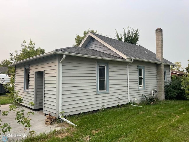 view of side of home with a shingled roof, a lawn, and a chimney