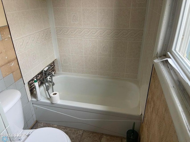 bathroom featuring a bathing tub, tile walls, and toilet