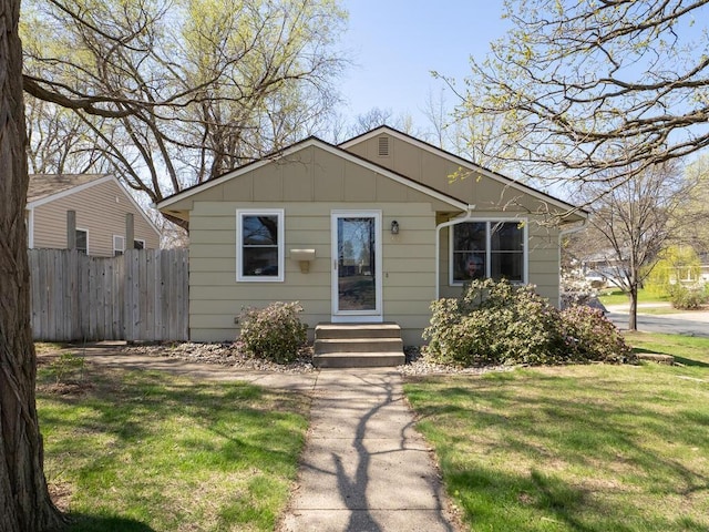 bungalow-style home featuring board and batten siding, fence, and a front yard