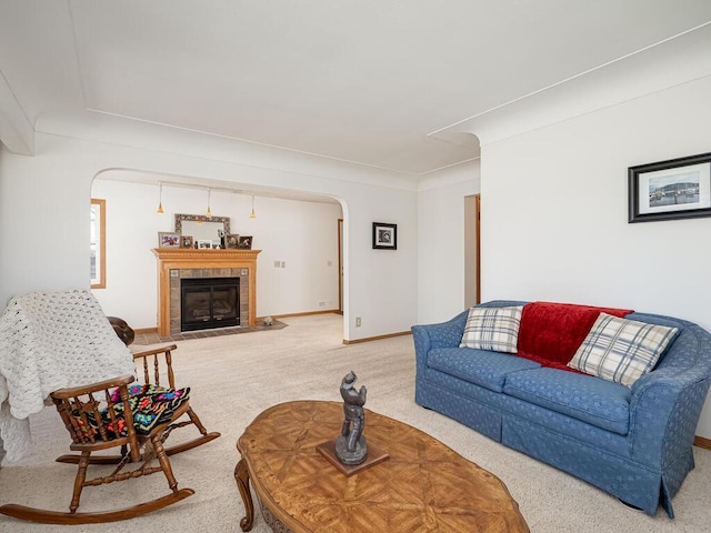 living area featuring arched walkways, carpet flooring, a tiled fireplace, and baseboards