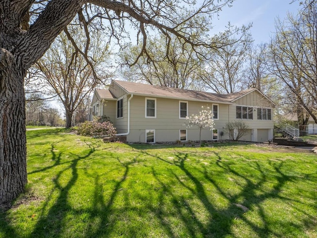 rear view of house featuring a lawn, board and batten siding, an attached garage, and stairs