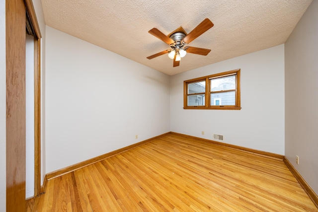 spare room with a textured ceiling, a ceiling fan, visible vents, light wood finished floors, and baseboards