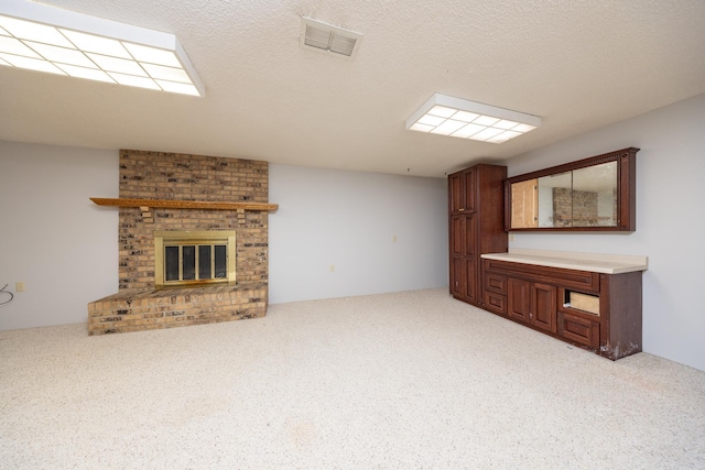 unfurnished living room featuring visible vents, light colored carpet, a textured ceiling, and a brick fireplace