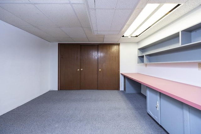 unfurnished office featuring built in desk, a drop ceiling, and carpet