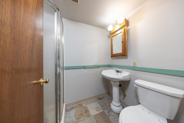 full bath featuring toilet, stone finish floor, a shower with door, and baseboards