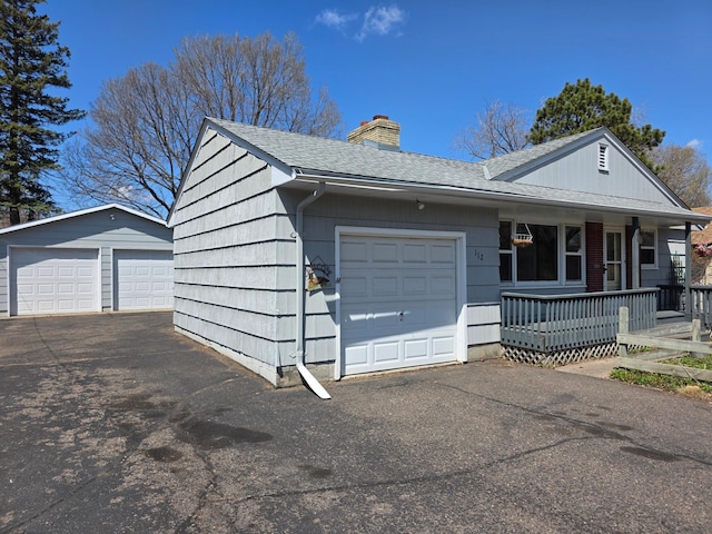 view of front of house featuring a detached garage, a shingled roof, a chimney, and covered porch