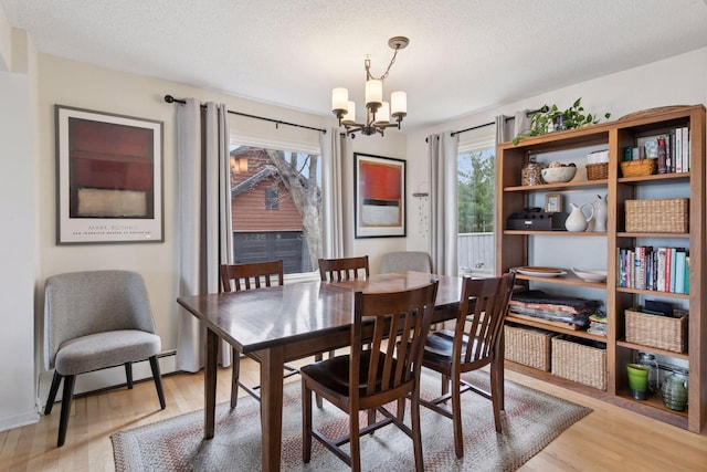 dining room featuring a textured ceiling, a chandelier, light wood-type flooring, and a baseboard heating unit