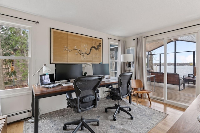 office area with a wealth of natural light, wood finished floors, and a baseboard radiator