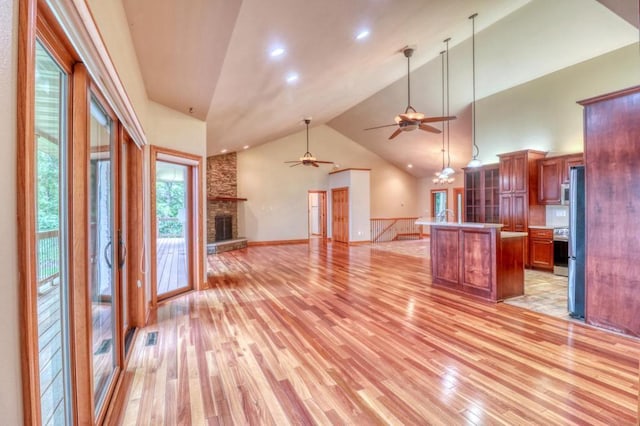 kitchen with a ceiling fan, open floor plan, a stone fireplace, and light wood-style floors
