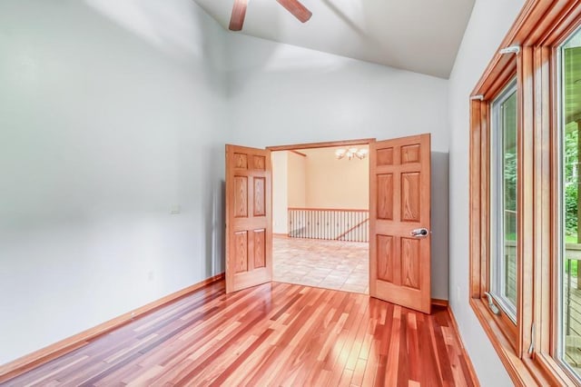 unfurnished room with high vaulted ceiling, ceiling fan with notable chandelier, and light wood-style flooring