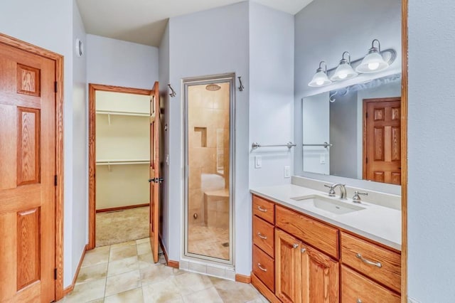 bathroom with a walk in closet, tile patterned flooring, vanity, baseboards, and a stall shower