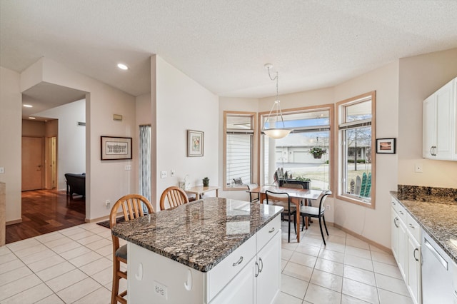 kitchen featuring light tile patterned floors, white cabinets, hanging light fixtures, a kitchen breakfast bar, and dark stone counters
