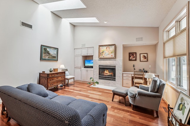 living area featuring high vaulted ceiling, light wood finished floors, a tiled fireplace, and visible vents