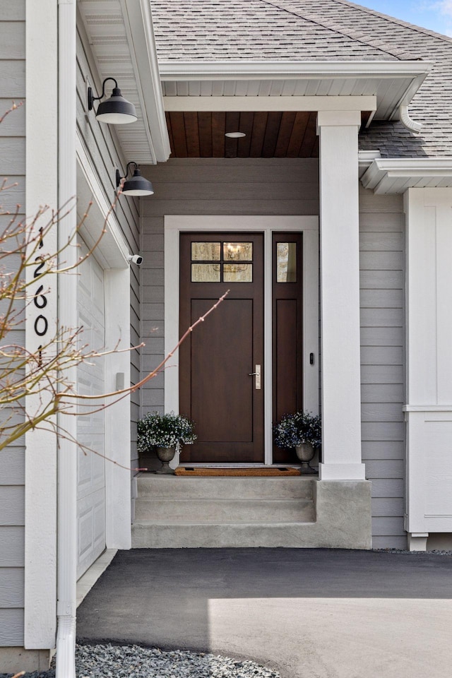 doorway to property featuring a porch and roof with shingles