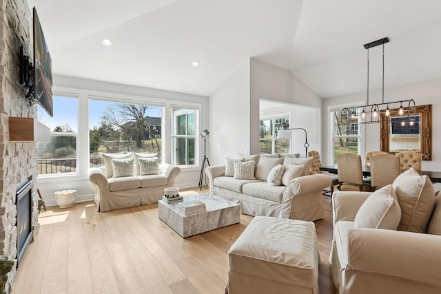 living room featuring a wealth of natural light, vaulted ceiling, light wood-type flooring, and a fireplace