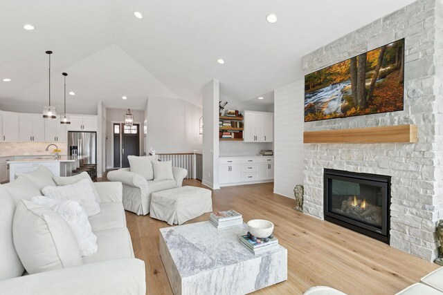 living room with vaulted ceiling, light wood-type flooring, a large fireplace, baseboards, and recessed lighting