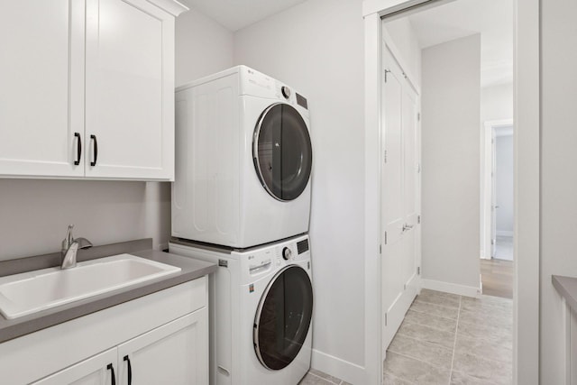 washroom with a sink, light tile patterned flooring, baseboards, cabinet space, and stacked washer and dryer