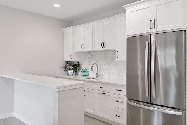 kitchen with light countertops, a sink, freestanding refrigerator, tasteful backsplash, and white cabinetry