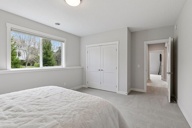 bedroom with baseboards, a closet, and light colored carpet