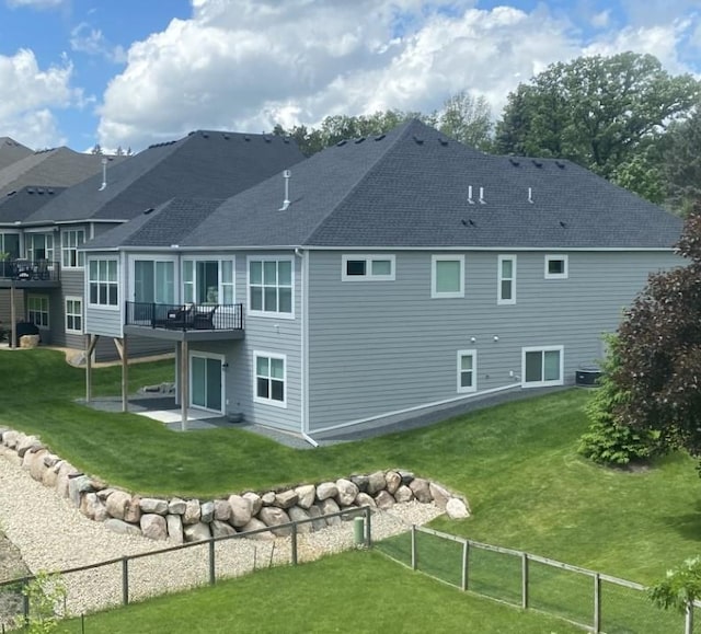 rear view of house with a patio area, a deck, a shingled roof, fence, and a yard