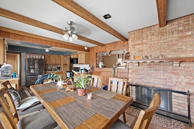 dining space with beamed ceiling, a fireplace, a ceiling fan, and wood finished floors