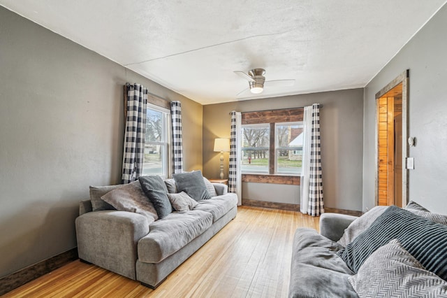 living room featuring a wealth of natural light, light wood finished floors, baseboards, and a ceiling fan