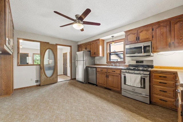 2591 Carver Ave E, Maplewood, MN 55119 - kitchen with stainless steel appliances, a ceiling fan, brown cabinetry, light countertops, and a textured ceiling