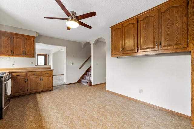 2591 Carver Ave E, Maplewood, MN 55119 - kitchen with a ceiling fan, brown cabinets, arched walkways, gas stove, and a textured ceiling