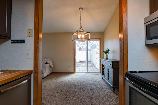 kitchen with lofted ceiling, appliances with stainless steel finishes, a textured wall, a chandelier, and carpet flooring