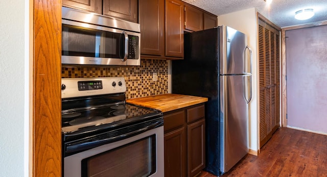 kitchen featuring dark wood-style flooring, a textured ceiling, wood counters, decorative backsplash, and appliances with stainless steel finishes