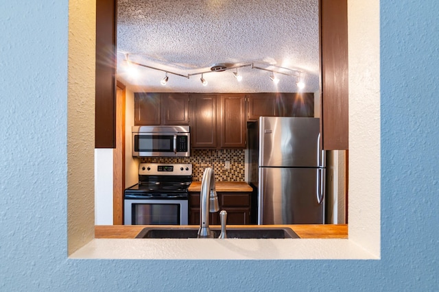 kitchen with tasteful backsplash, a sink, a textured wall, stainless steel appliances, and light countertops