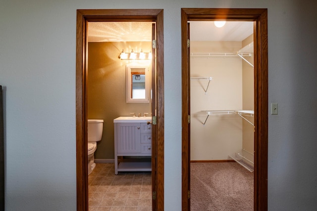 bathroom with baseboards, a spacious closet, toilet, and vanity