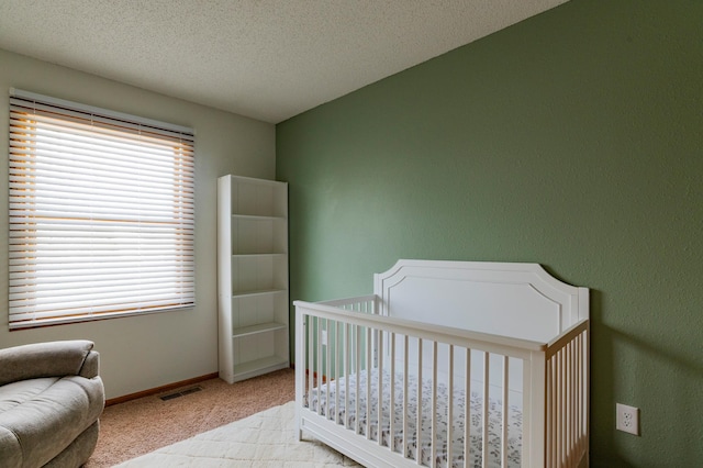 bedroom with a nursery area, a textured ceiling, carpet floors, baseboards, and visible vents