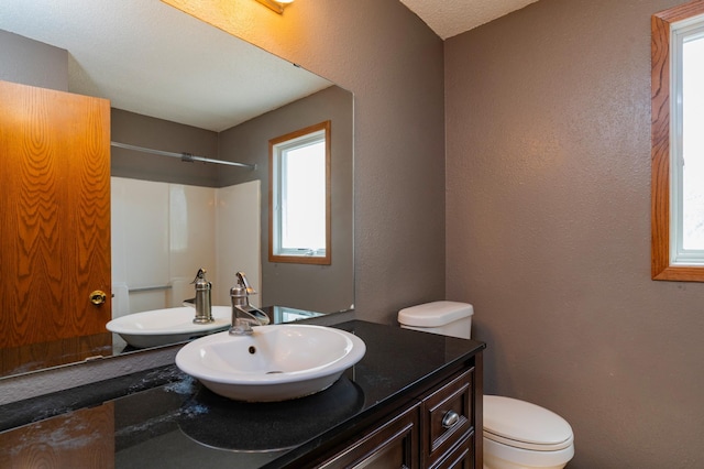bathroom with a textured wall, vanity, a shower, and toilet