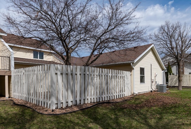 view of side of property featuring fence, a lawn, and central AC unit