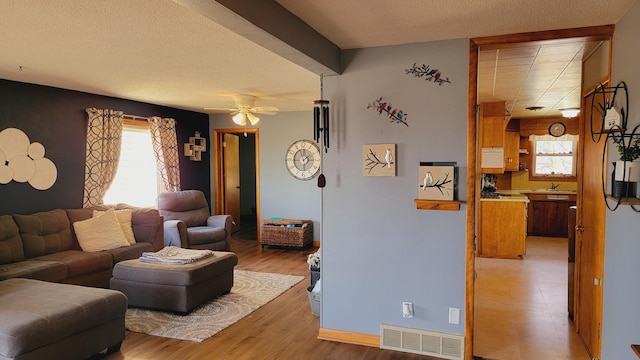 living area with visible vents, baseboards, a ceiling fan, a textured ceiling, and light wood-style flooring