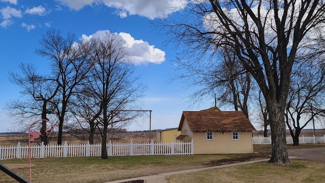 view of side of property with roof with shingles, an outbuilding, a fenced front yard, and a lawn