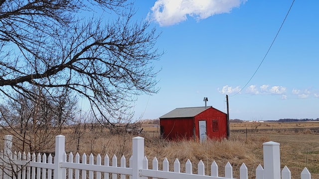view of yard featuring a rural view, an outdoor structure, fence, and a storage unit