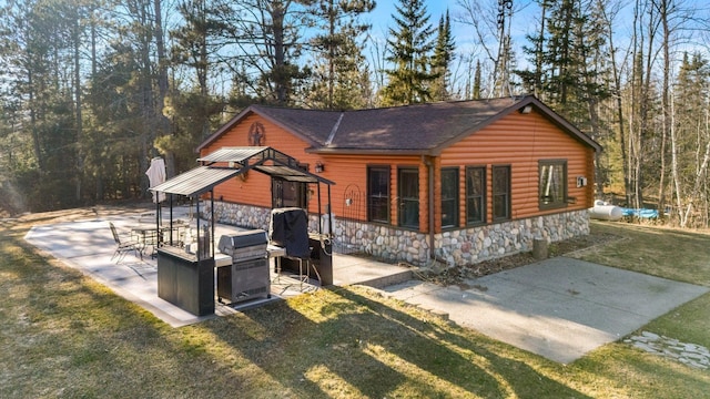 rear view of house featuring a yard, a patio area, and stone siding