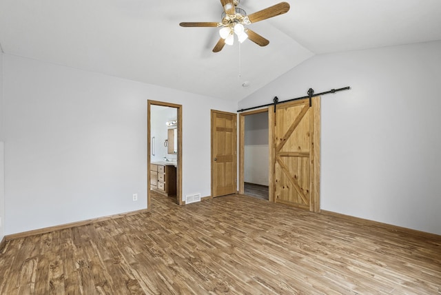 unfurnished bedroom with visible vents, vaulted ceiling, a barn door, and wood finished floors