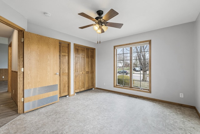 unfurnished bedroom featuring multiple closets, a ceiling fan, and baseboards