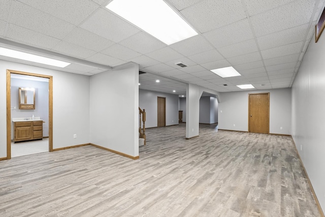 below grade area featuring light wood finished floors, visible vents, baseboards, and a paneled ceiling
