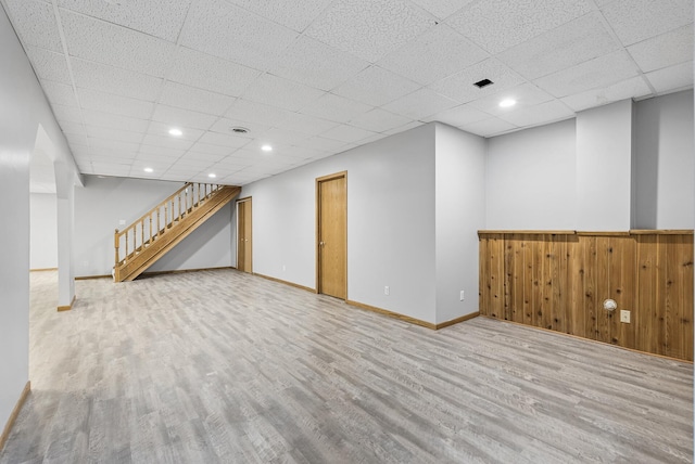 finished below grade area featuring recessed lighting, a drop ceiling, wood finished floors, and stairs