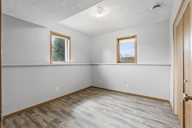 unfurnished room featuring baseboards, a textured ceiling, a wainscoted wall, visible vents, and wood finished floors