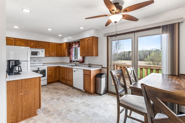 kitchen with brown cabinetry, stone finish flooring, a sink, light countertops, and white appliances